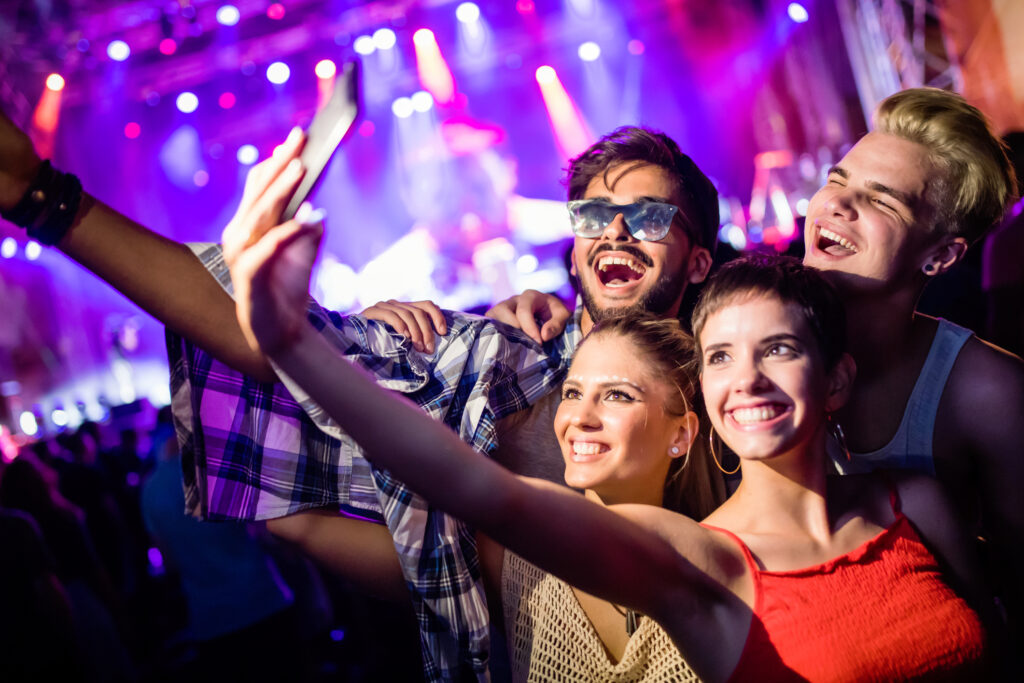 group of four friends taking a selfie at a lively concert